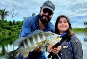 pai com filhos segurando peixe tucunaré