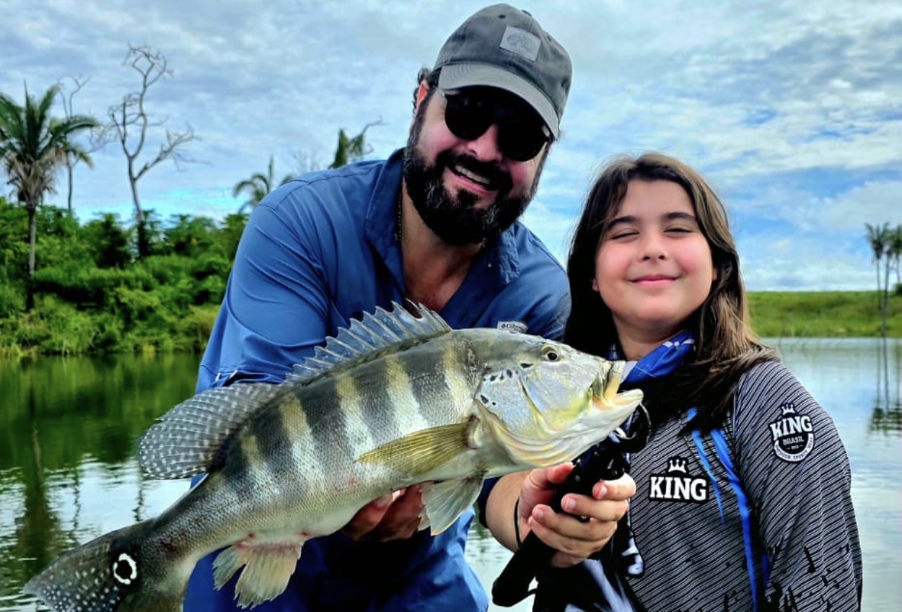 pai com filhos segurando peixe tucunaré